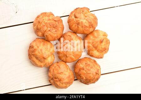 Diverse chouquettes fresche profumate, primo piano, su un tavolo di legno bianco, vista dall'alto. Foto Stock