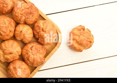 Diverse chouquettes fresche fragranti in una piastra di bambù, primo piano, su un tavolo di legno bianco, vista dall'alto. Foto Stock