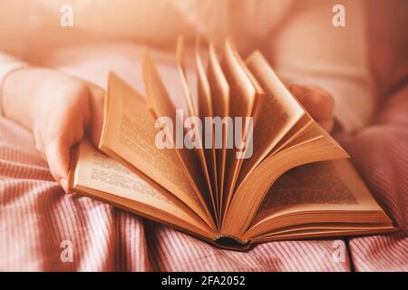 Un uomo in un maglione bianco è sdraiato su un letto con una coperta rosa a strisce e che si capovolgeva attraverso le pagine di un vecchio libro interessante. Auto-sviluppo. Re Foto Stock