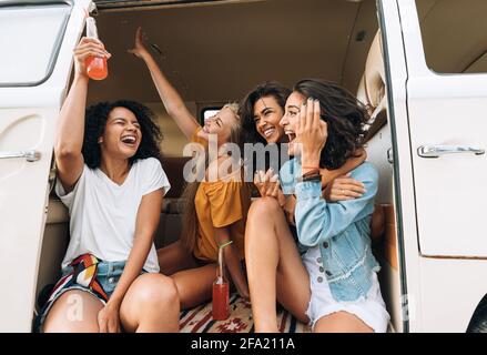 Gruppo multietnico di donne che si aggirano durante il viaggio. Amici in van alzando le mani e ridendo. Foto Stock