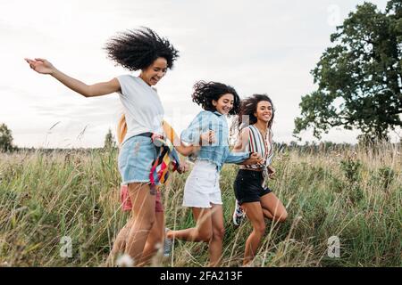 Quattro donne che tengono le mani che corrono sul campo. Ridere amici divertirsi all'aperto in estate. Foto Stock