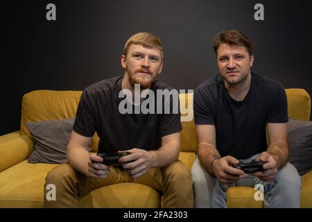 due allegri bei ragazzi giocare appassionatamente video gioco che tiene la console gamepad Foto Stock