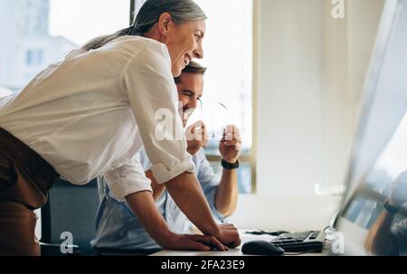 Manager donna con collega che controlla lo stato del progetto sul computer. donna d'affari e uomo d'affari che guarda il computer e sorride. Foto Stock