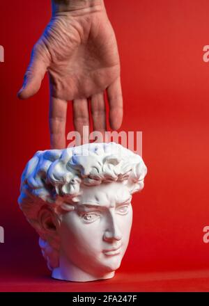 Vaso in gesso sotto forma di testa di Davide e mano maschio su sfondo rosso. Foto Stock