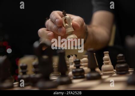 Uomo che prende il passo successivo sul gioco degli scacchi. Mano umana che muove il re degli scacchi bianchi di legno Foto Stock