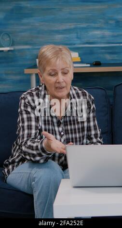 Eccitata coppia senior sorridente che guarda il computer portatile ondeggiando durante la videocall seduto sul divano. Allegro marito pensionato e moglie ridendo parlare a riunione virtuale riposarsi sul divano in una stanza accogliente. Foto Stock