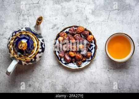 Cibo popolare durante Iftar - datteri asciutti, teiera, ciotola con tè nero su sfondo concreto Vista superiore Flat Lay musulmano vacanza del mese santo di Ramadan Foto Stock