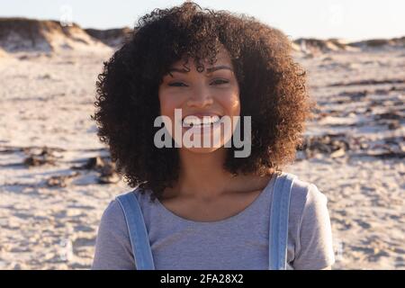 Ritratto di donna afroamericana guardando la macchina fotografica e sorridendo in spiaggia Foto Stock