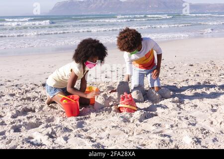 Madre afroamericana con il figlio che indossa maschera di gioco con sabbia in spiaggia Foto Stock