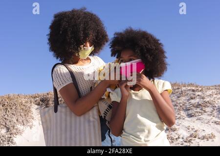 Madre afroamericana con figlia che mette la maschera di faccia sopra a. la spiaggia Foto Stock