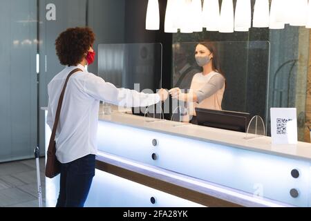 Uomini d'affari diversi che indossano una maschera che parla con l'addetto alla reception dell'hotel Foto Stock