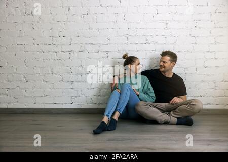 giovane coppia felice seduta sul pavimento accanto alla parete in camera vuota. passaggio a un nuovo concetto di casa. copia spazio Foto Stock