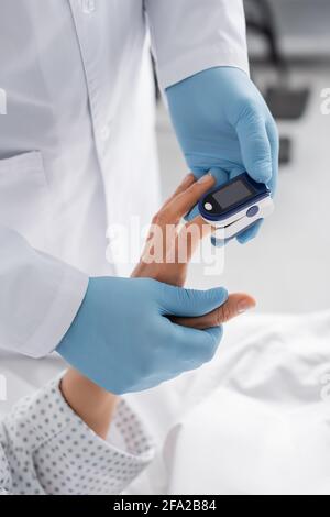 vista ritagliata del medico in guanti in lattice che misura la frequenza cardiaca di donna con pulsossimetro Foto Stock