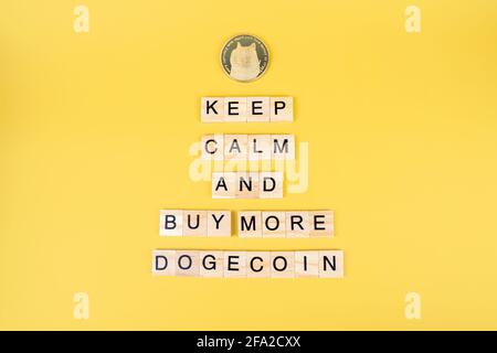 Mantenere la calma e acquistare di più Dogecoin, divertente segno sulla criptovaluta con blocchi di legno e moneta con la faccia del cane su sfondo giallo. Doge prezzo aumento con Foto Stock