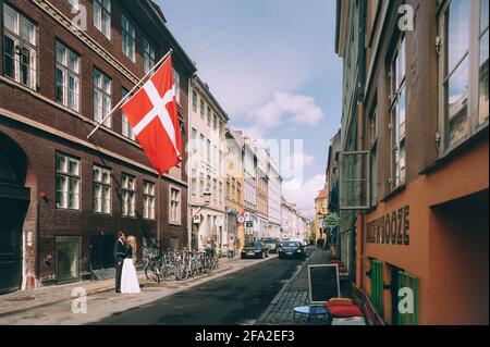 Copenaghen, Danimarca 11 giugno 2019. Coppia di nozze che camminano lungo la strada sullo sfondo della bandiera della Danimarca. Foto Stock