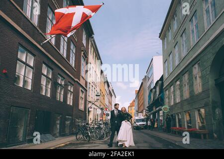 Copenaghen, Danimarca 11 giugno 2019. Coppia di nozze che camminano lungo la strada sullo sfondo della bandiera della Danimarca. Foto Stock