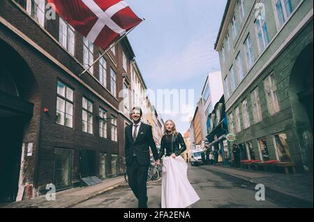 Copenaghen, Danimarca 11 giugno 2019. Coppia di nozze che camminano lungo la strada sullo sfondo della bandiera della Danimarca. Foto Stock