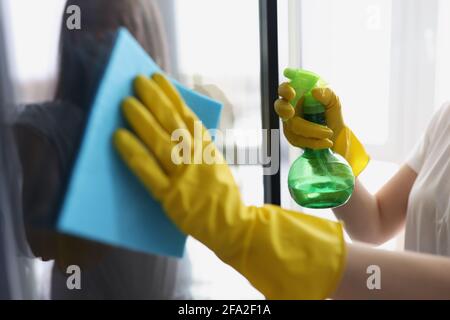 Le mani femminili in guanti gialli lavano le finestre con straccio e. detergente Foto Stock