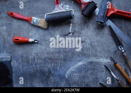 Concetto di strumenti di linea. Strumenti di lavoro in rosso e nero su tavolo scuro con spazio di copia. Strumenti di taglio, rullo d'inchiostro e altri utensili per la produzione di linocut. Foto di alta qualità Foto Stock