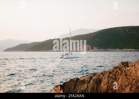 Yacht a vela bianco naviga sul mare passando per la montagna costa Foto Stock