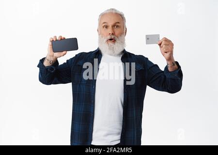 Un uomo anziano sorpreso che mostra lo schermo dello smartphone e la carta di credito, che fa il gasting e dice wow. Un uomo maturo entusiasta che consiglia l'app per lo shopping online, senza contatto Foto Stock