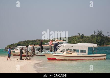 Uomini d'affari giapponesi a bordo di una piccola barca ormeggiata in acque turchesi sul bordo di sabbia bianca a Kabira Bay, Isola di Ishigaki, Okinawa, Giappone Foto Stock