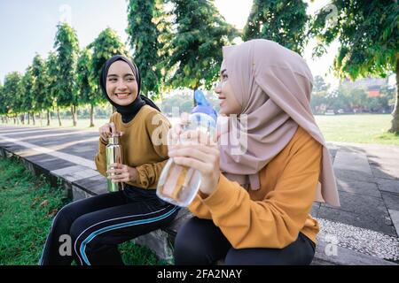 Primo piano di due ragazze musulmane felici dopo gli sport insieme nel pomeriggio quando rompere l'acqua veloce e potabile utilizzo di flaconi Foto Stock