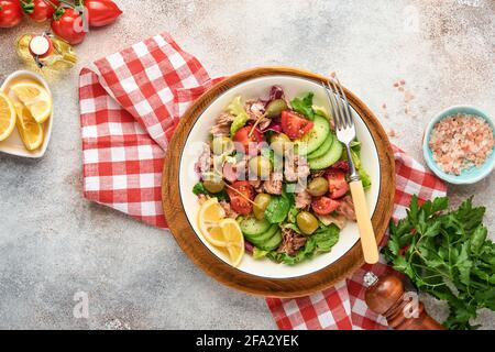 Insalata di tonno con verdure fresche, olive, capperi e limone servita in ciotola su fondo grigio chiaro. Vista dall'alto con spazio per la copia. Foto Stock