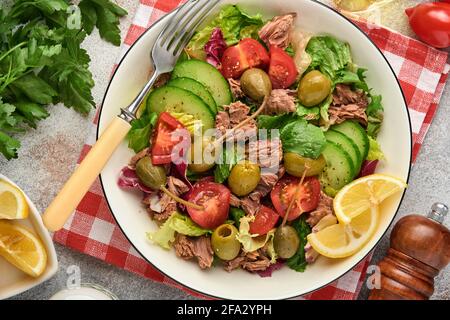 Insalata di tonno con verdure fresche, olive, capperi e limone servita in ciotola su fondo grigio chiaro. Vista dall'alto con spazio per la copia. Foto Stock