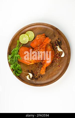 Gamba di pollo marinata senza pelle disposta su una base di legno e guarnita con fette di limone, spezie, foglie di coriandolo, spicchi d'aglio e pepe su p. Foto Stock