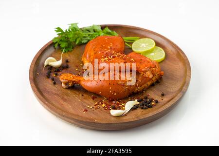 Gamba di pollo marinata senza pelle disposta su una base di legno e guarnita con fette di limone, spezie, foglie di coriandolo, spicchi d'aglio e pepe su p. Foto Stock