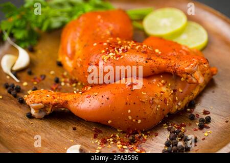 Coscia di pollo marinata senza pelle disposta su base di legno e guarnita con fette di limone, spezie, foglie di coriandolo, spicchi d'aglio e pepe su g. Foto Stock