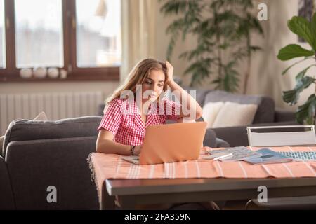 Studente biondo esausto che ha una classe in linea a casa mentre sognando di dormire sul divano che la colgono. Foto Stock