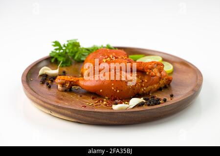 Gamba di pollo marinata senza pelle disposta su una base di legno e guarnita con fette di limone, spezie, foglie di coriandolo, spicchi d'aglio e pepe su p. Foto Stock