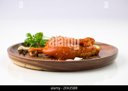 Gamba di pollo marinata senza pelle disposta su una base di legno e guarnita con fette di limone, spezie, foglie di coriandolo, spicchi d'aglio e pepe su p. Foto Stock