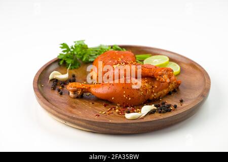 Gamba di pollo marinata senza pelle disposta su una base di legno e guarnita con fette di limone, spezie, foglie di coriandolo, spicchi d'aglio e pepe su p. Foto Stock