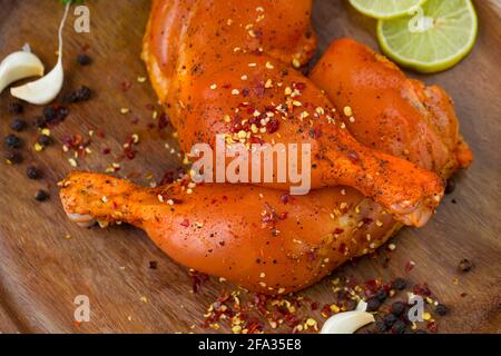 Coscia di pollo marinata senza pelle disposta su base di legno e guarnita con fette di limone, spezie, foglie di coriandolo, spicchi d'aglio e pepe su g. Foto Stock