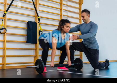 coppia di un addestratore personale sorridente ed una donna incinta bella che fa l'esercitazione indoor.girl che solleva il peso in una sessione della palestra dentro. misura, Foto Stock