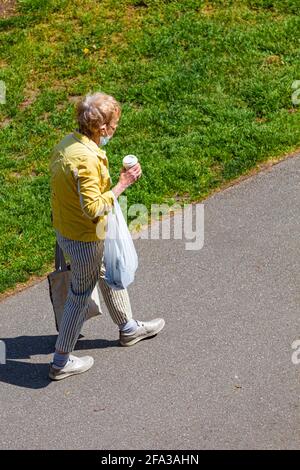 Donna anziana che porta la sua tazza di caffè e borse lungo un Percorso in Steveston British Columbia Canada Foto Stock