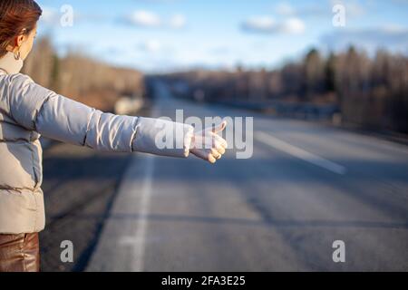 La ragazza ferma la macchina in autostrada con la mano. La donna elegante in viaggio ferma l'auto in viaggio. Una strada nel mezzo della foresta. Foto Stock