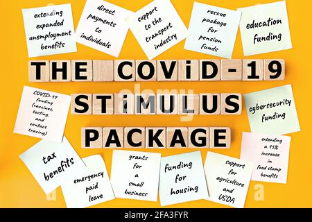 Foto sul tema del pacchetto Stimulus COVID-19. Cubi di legno con l'iscrizione 'il pacchetto Stimulus COVID-19', e note appiccicose, su sfondo giallo Foto Stock