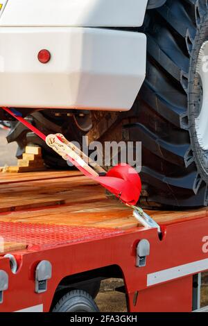 Frammento di fissaggio di un veicolo industriale per impieghi gravosi con una cinghia di montaggio su una piattaforma di trasporto. Immagine verticale, spazio di copia. Foto Stock