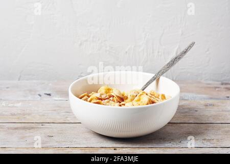 Fiocchi di mais in una ciotola bianca su un tavolo di legno. Cereali con latte. Foto Stock
