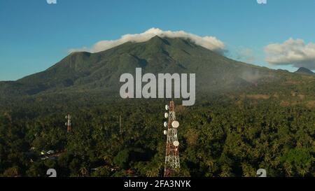 Torre di telecomunicazione, antenna di comunicazione contro le montagne e la foresta pluviale, vista aerea. Ripetitori su una torre di metallo. Camiguin, Filippine Foto Stock