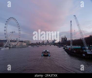 Londra, Grande Londra, Inghilterra - Aprile 17 2021: Barca sul Tamigi in avvicinamento al tramonto con il London Eye sulla sinistra e il Westminster Bridge. Foto Stock