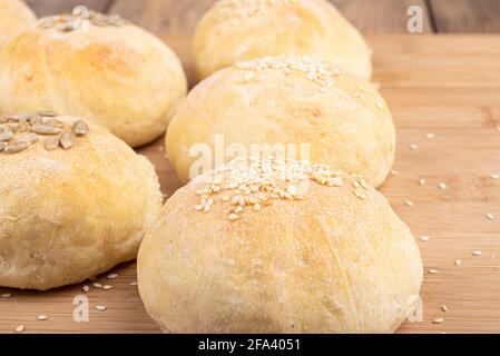 Focalizzazione selettiva su focacce fatte in casa con semi di sesamo e girasole. Mettere a fuoco il primo piano. Panini appena sfornati su un tagliere. Foto Stock