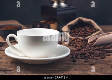 Una tazza di ceramica bianca vuota sullo sfondo dei chicchi di caffè e un macinacaffè. Immagine colorata. Foto Stock