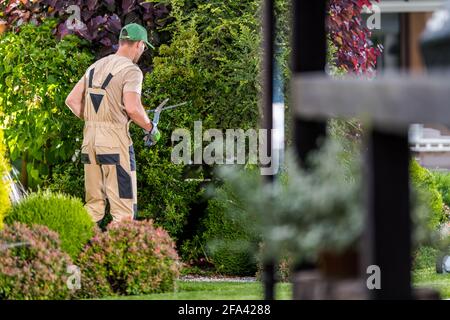 Caucasian Garden Worker nei suoi 40 impianti di rifilatura durante la manutenzione stagionale di primavera. Giardinaggio e giardinaggio. Foto Stock