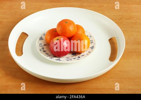 Vassoio di plastica bianca con mele e mandarini in un piatto su un tavolo di legno. Primo piano Foto Stock