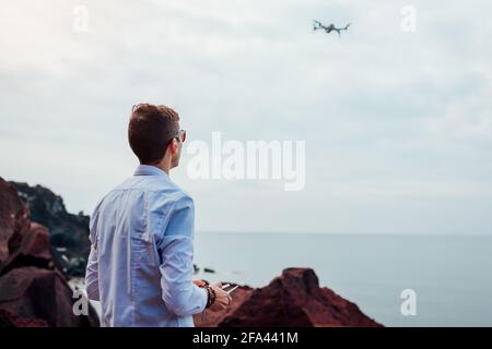 Telecomando drone. Videografo che aziona il controller del copter via mare. Riprese aeree di Red Beach sull'isola di Santorini. Foto Stock